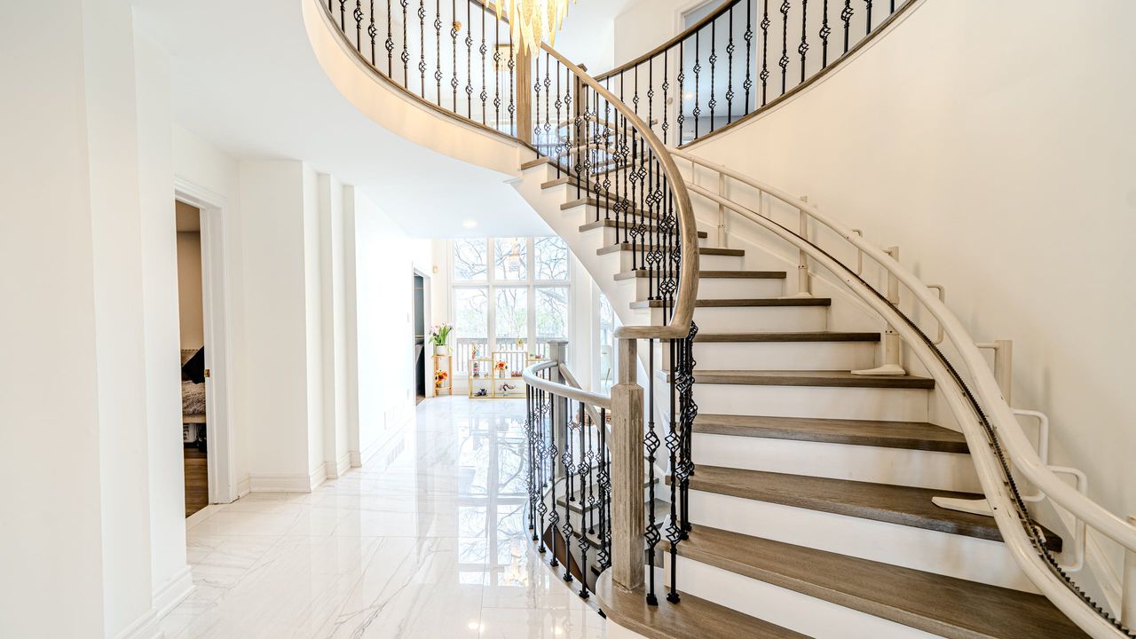 Foyer with a curved staircase, grey wood treads, white risers, iron balusters and glossy white tile floor