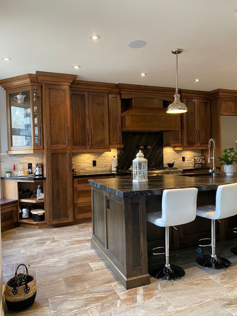 Brown stained kitchen with a black granite island, stacked stone backsplash and a wood range hood