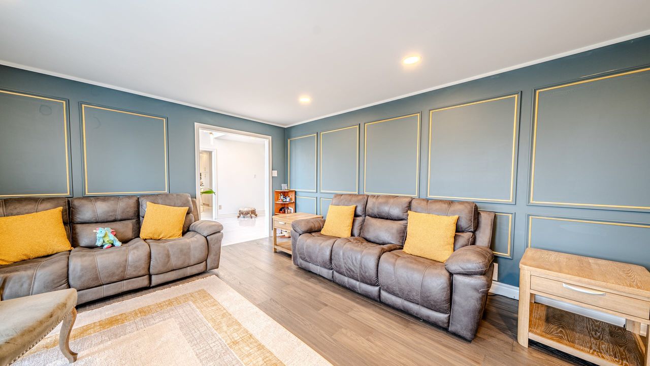 Living room with deep teal walls, gold trimmed box moulding, white ceiling and trim, pot lights and plank flooring