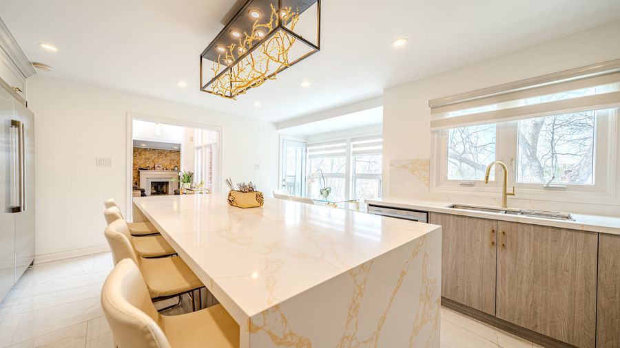 Kitchen with a gold veined quartz waterfall island, cream bar stools, grey wood grain cabinets and a brass faucet