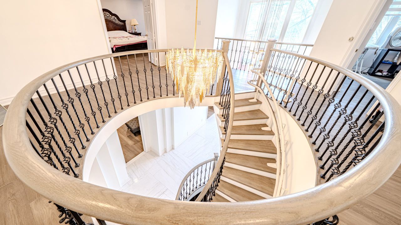 View down a curved staircase from the upper landing, with wood treads, an oval wood handrail and iron balusters