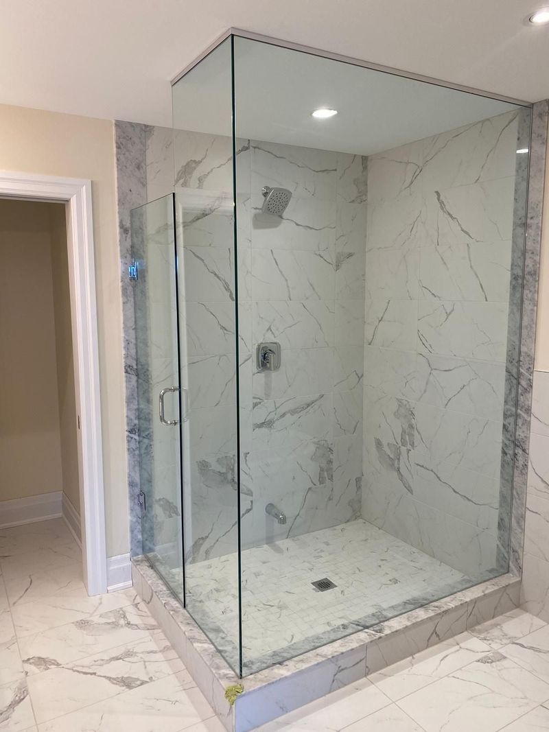 Frameless glass shower with marble-look porcelain walls, mosaic floor and a marble curb