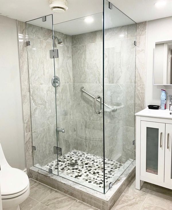 Glass corner shower with grey marble-look tile, pebble mosaic floor and a white vanity