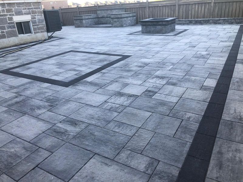 Backyard interlock patio with charcoal border inlays, a stone fire pit and built-in seating walls