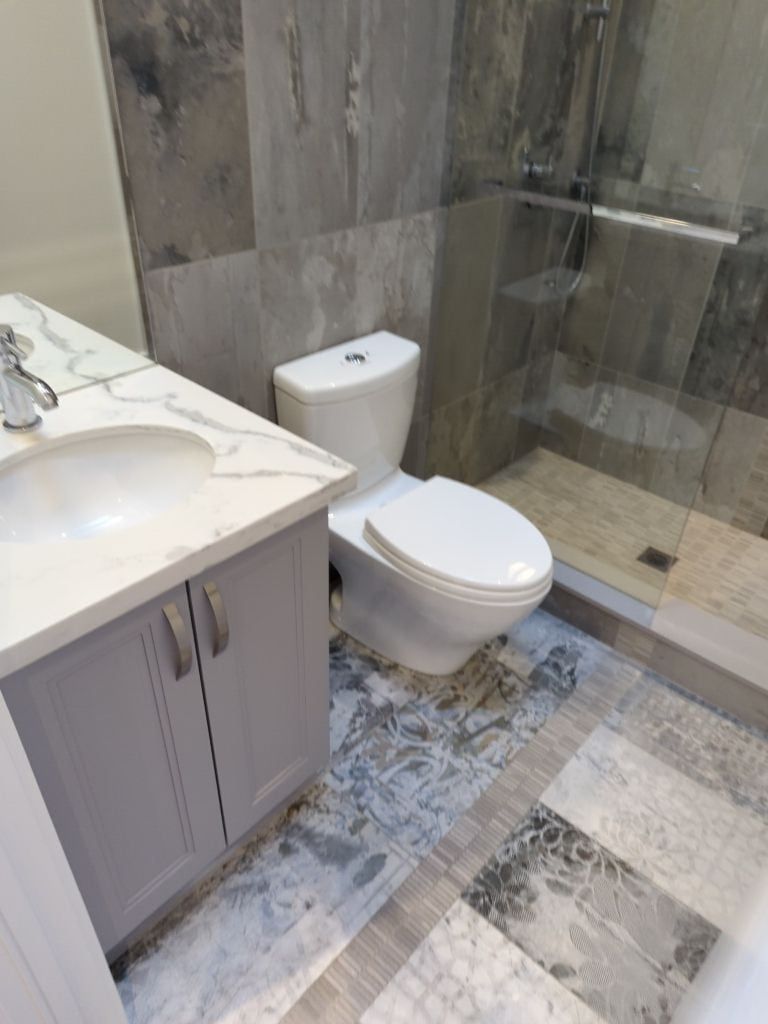 Bathroom with a grey shaker vanity, quartz top, patterned floor tile and a glass shower in grey stone look tile