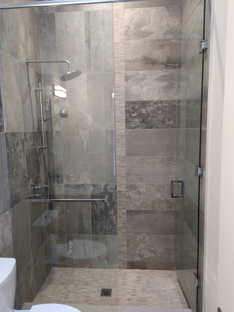 Glass shower with grey stone look tile, a vertical mosaic accent strip, rain head, slide bar and mosaic floor