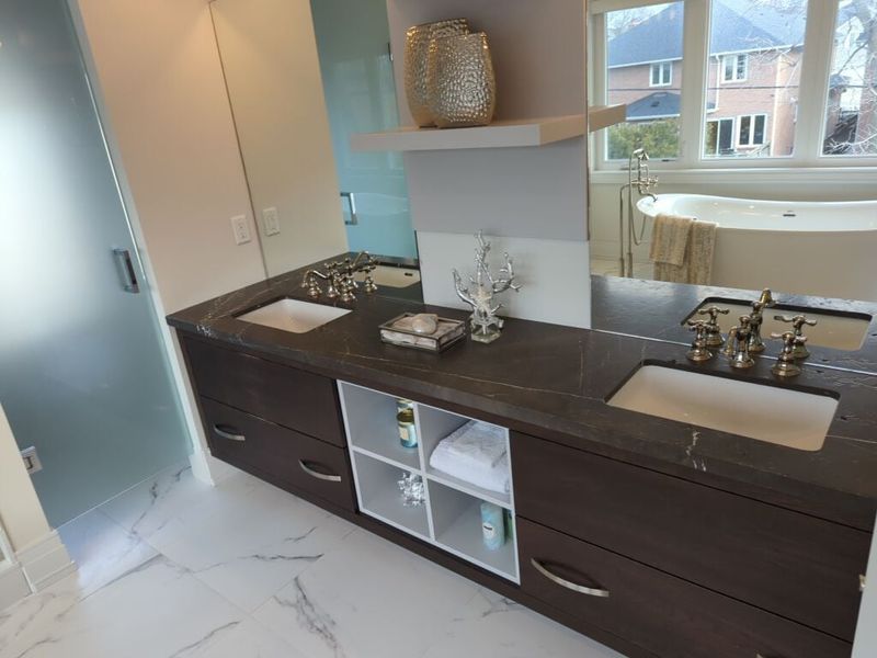 Dark wood double vanity with a dark stone top, open cubby storage, a wide mirror and a floating shelf