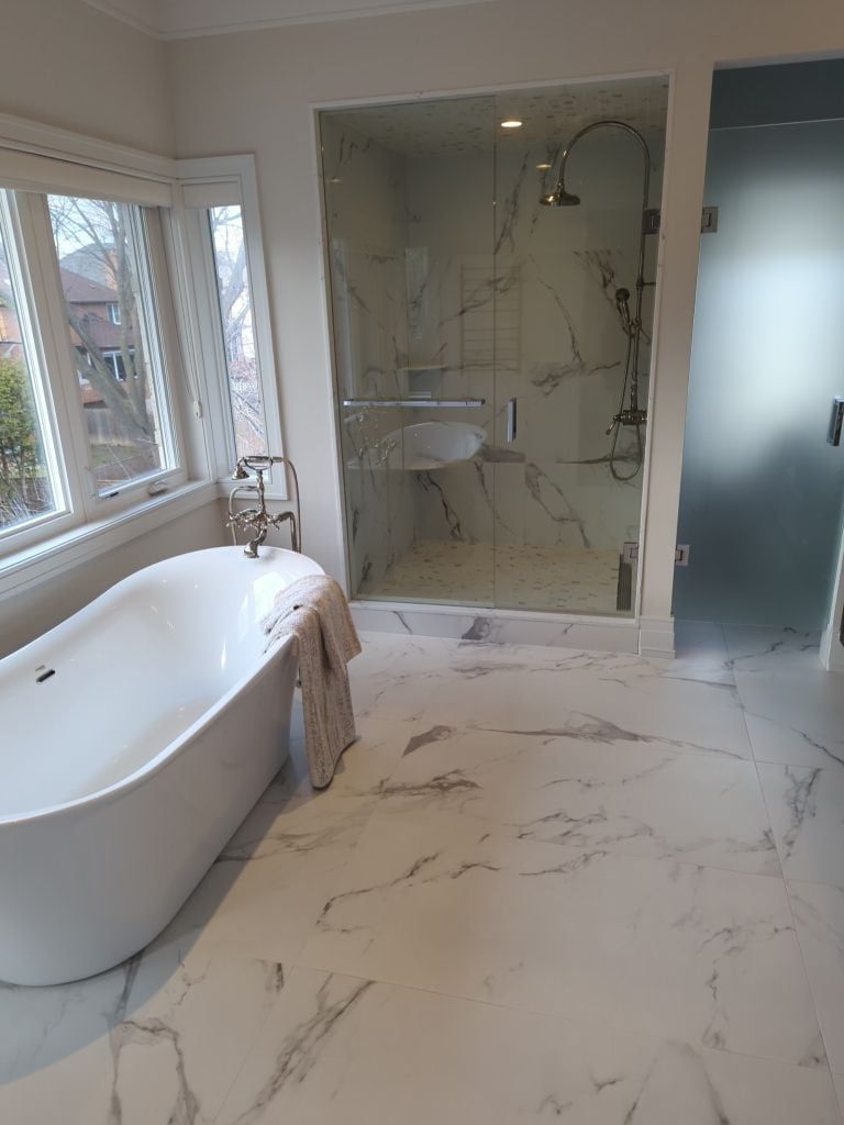 Ensuite with a freestanding tub, a glass shower in marble look tile and large marble look floor tile