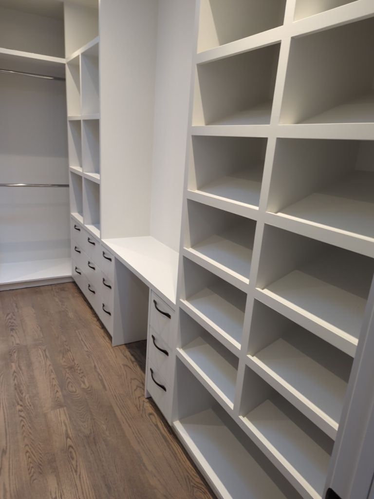 Walk-in closet with white cubby shelving, drawer banks, a counter ledge and hanging rods on hardwood floors