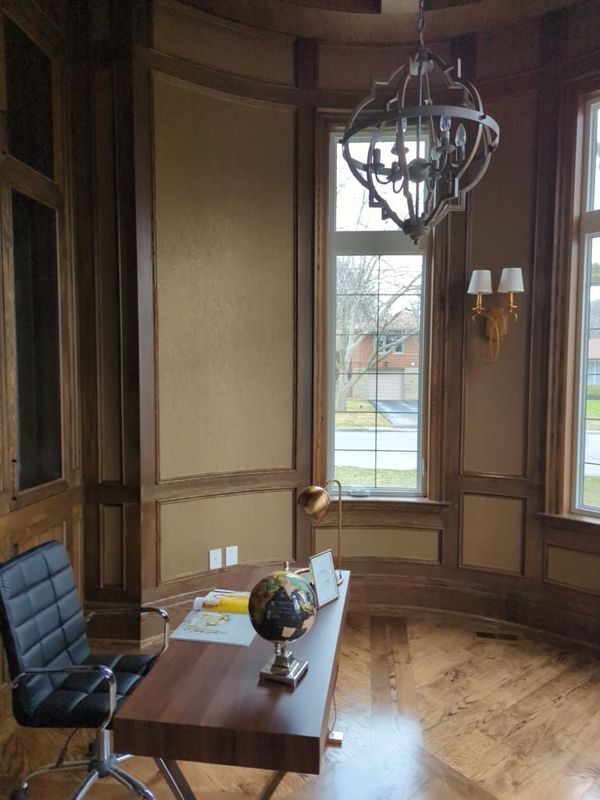 Round home office with stained wood wall panelling, tall windows, brass wall sconces and patterned hardwood