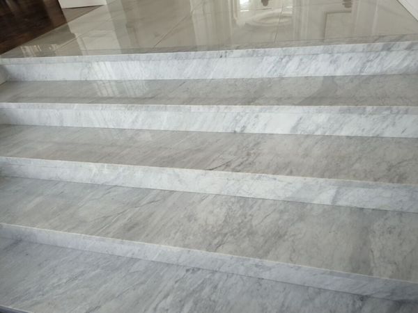 Wide white marble stairs with grey veining and square nosings leading up to polished floor tile