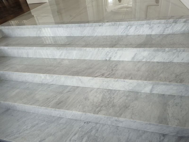 Wide white marble stairs with grey veining and square nosings leading up to polished floor tile