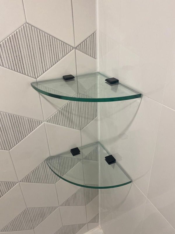 Glass corner shelves with black clips on white and grey geometric shower tile