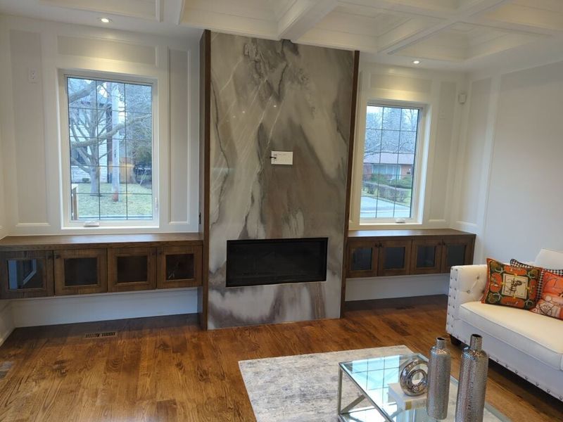 Living room with a full height stone slab fireplace wall, stained oak window benches and a coffered ceiling