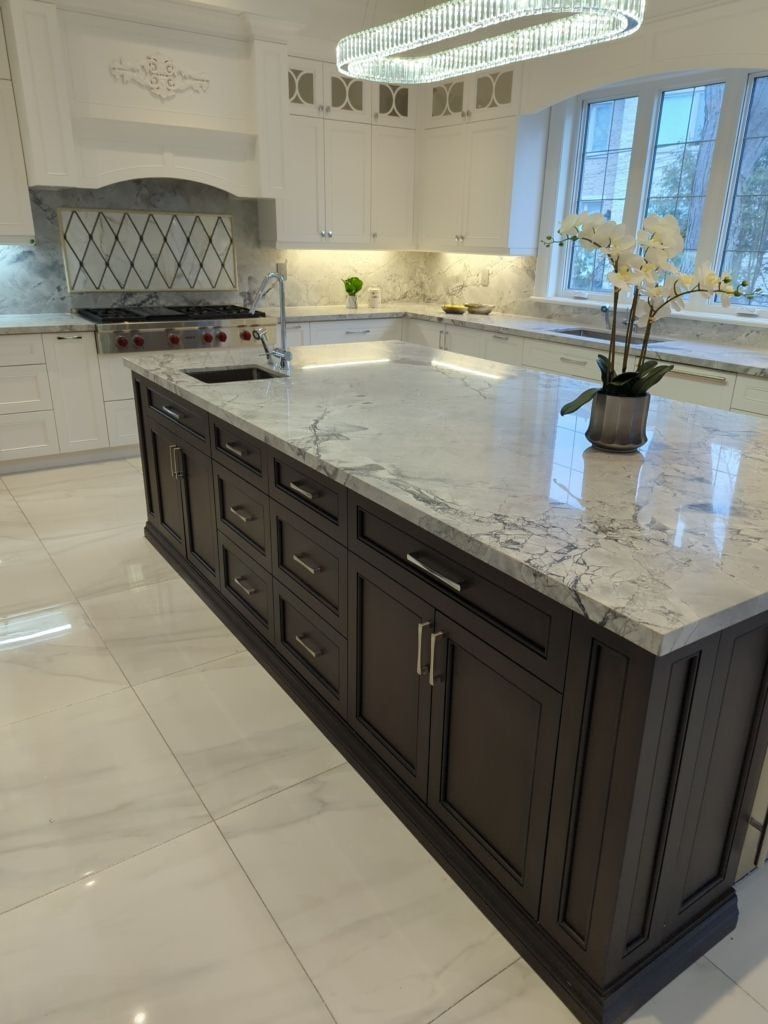 Dark wood kitchen island with a thick quartzite top facing white shaker cabinets and marble look floors