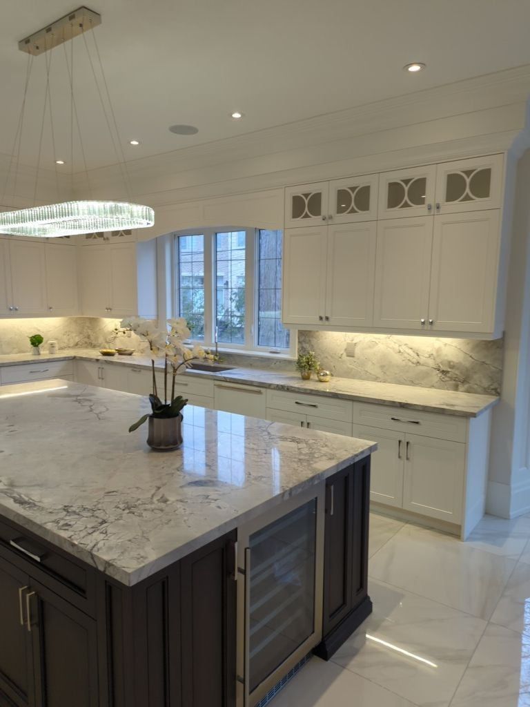 White kitchen with under-cabinet lighting, a quartzite island with a wine fridge and a crystal pendant