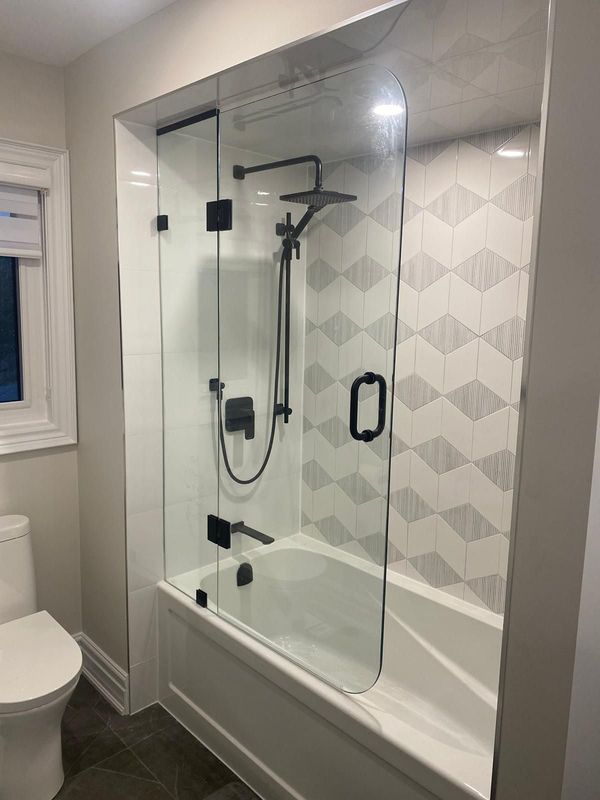 Tub with a hinged glass screen, matte black fixtures and geometric grey and white tile