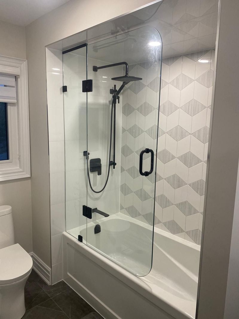 Tub with a hinged glass screen, matte black fixtures and geometric grey and white tile