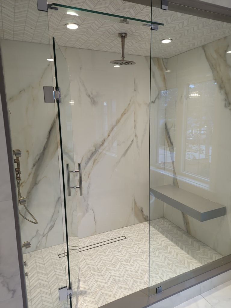 Glass shower with marble look slab walls, a chevron tile ceiling, a rain head and a floating bench