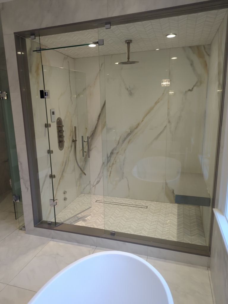 Floor to ceiling glass steam shower with marble look slab walls and a chevron mosaic floor and ceiling