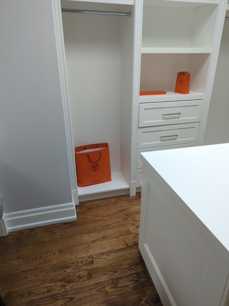 Walk-in closet with white shelving, a drawer tower, hanging rods and an island on hardwood floors