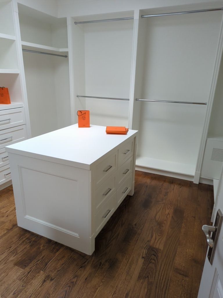 Walk-in closet with a white shaker drawer island, double hanging rods and stained hardwood floors