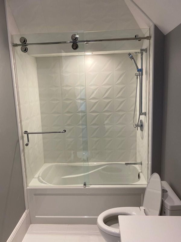 Bathtub with a sliding glass door, white three-dimensional wall tile and a handheld shower rail
