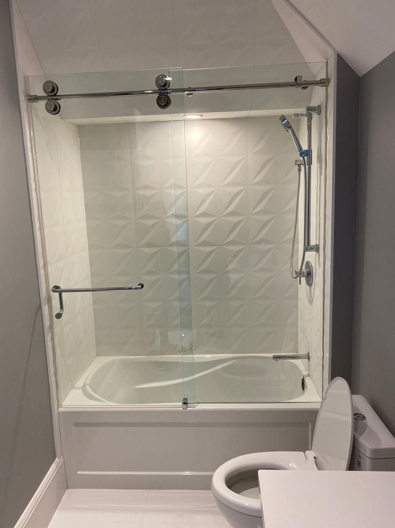 Bathtub with a sliding glass door, white three-dimensional wall tile and a handheld shower rail