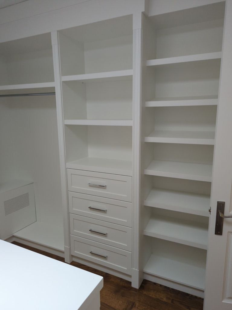 Walk-in closet wall with white adjustable shelving, a four drawer bank and a hanging section