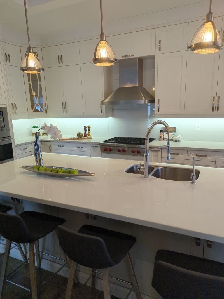 Kitchen with white shaker cabinets, quartz island, undermount sink, pendant lights and stainless chimney hood
