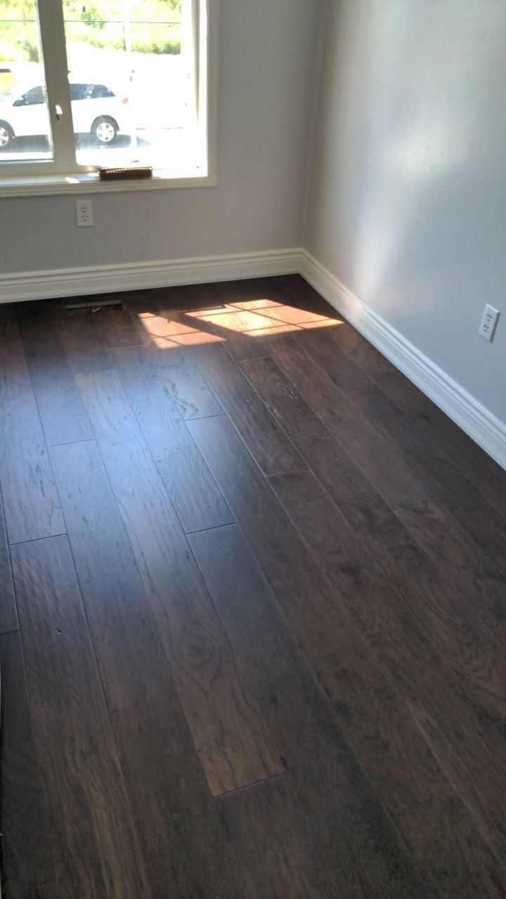 Bedroom with dark hand-scraped hardwood floor, white baseboards and light grey walls