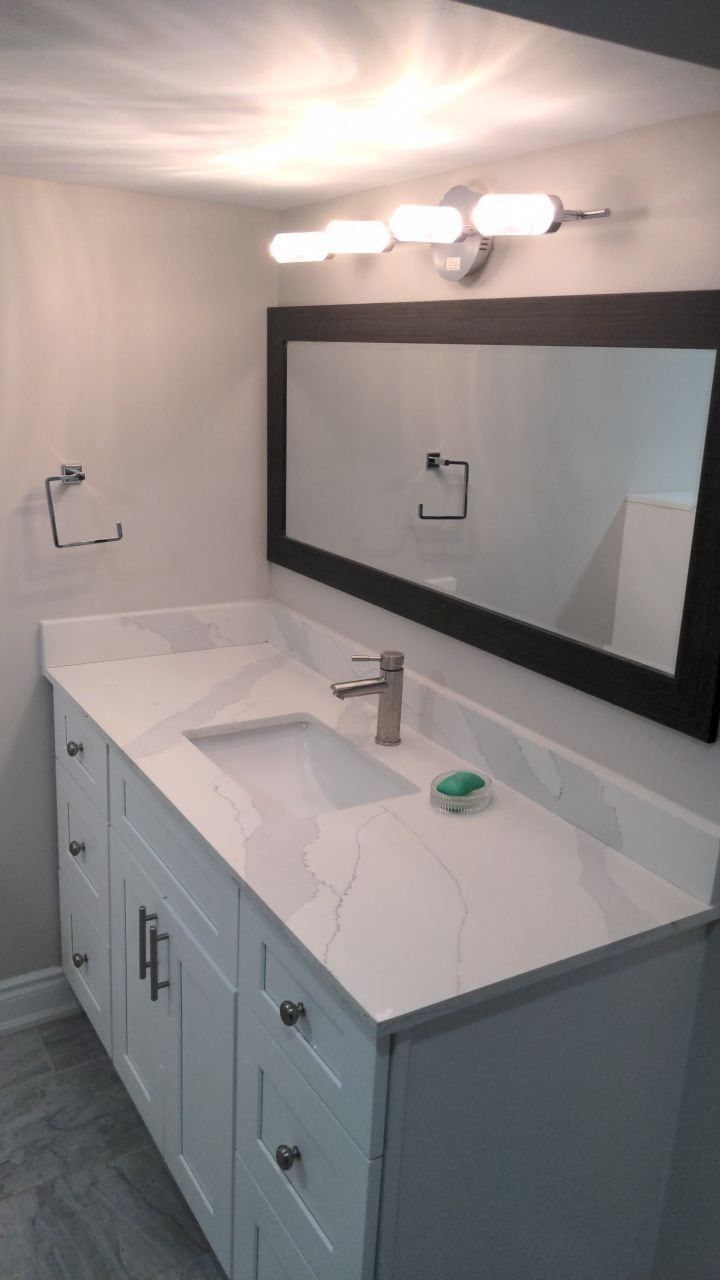 Bathroom vanity with white shaker cabinets, white quartz top, undermount sink and dark framed mirror