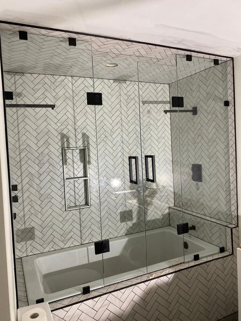 Glass enclosure over a soaker tub with white herringbone tile and matte black hardware
