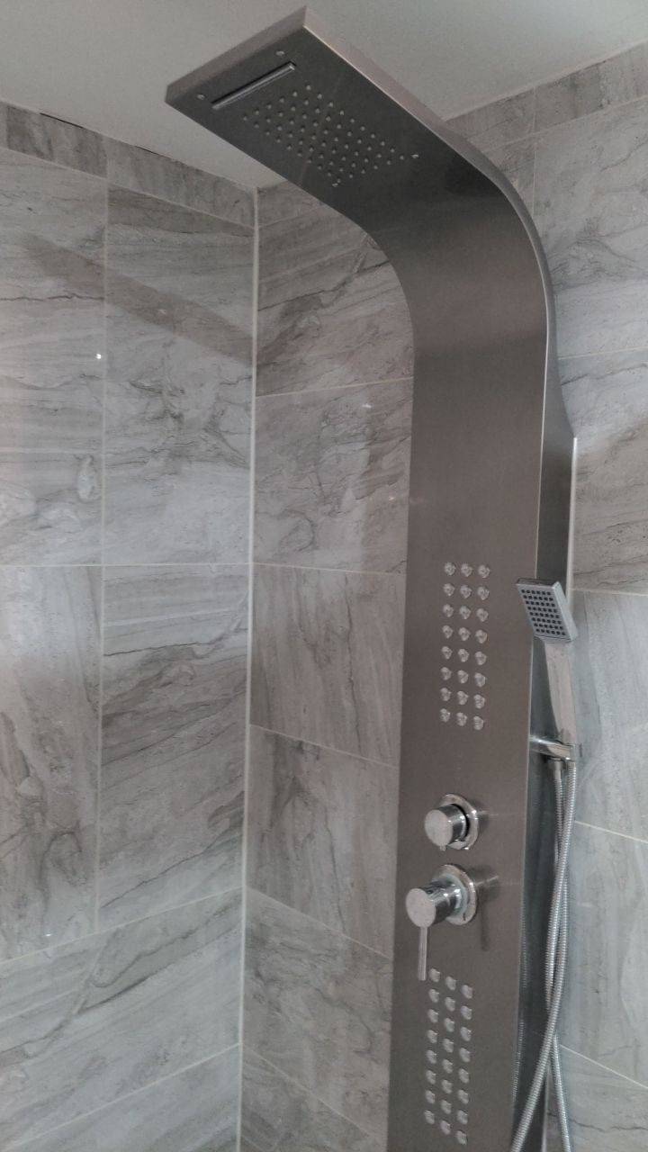 Stainless steel shower tower with rain head, body jets and handheld spray on grey marble-look tile