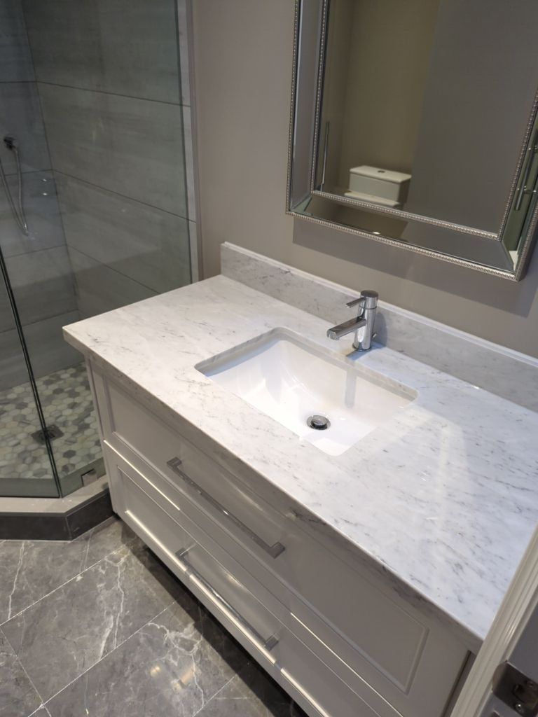 Bathroom vanity with white marble top, undermount sink and beaded silver mirror beside a glass shower