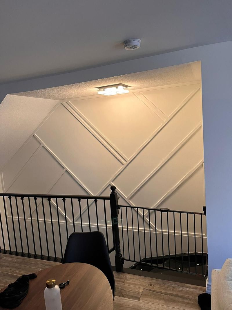 White geometric trim accent wall above a stairwell with black metal spindle railing