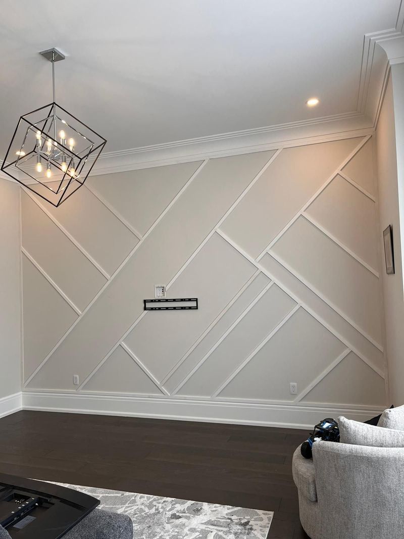 Living room accent wall with white diagonal trim panels, crown moulding and cube chandelier