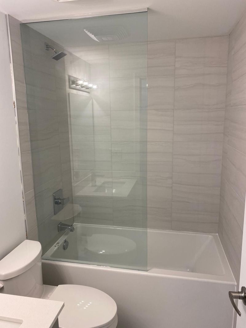 Bathtub with a fixed glass panel and grey linear porcelain tile from tub to ceiling