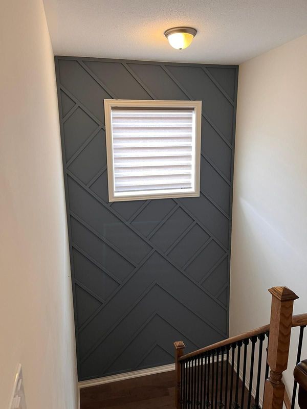 Charcoal geometric trim accent wall around a window above a staircase with oak newel post
