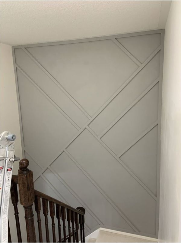 Grey geometric trim accent wall in a stairwell above a dark stained wood railing