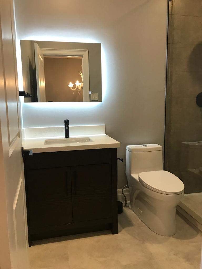Bathroom with backlit LED mirror, dark wood-grain vanity, white quartz top and one-piece toilet