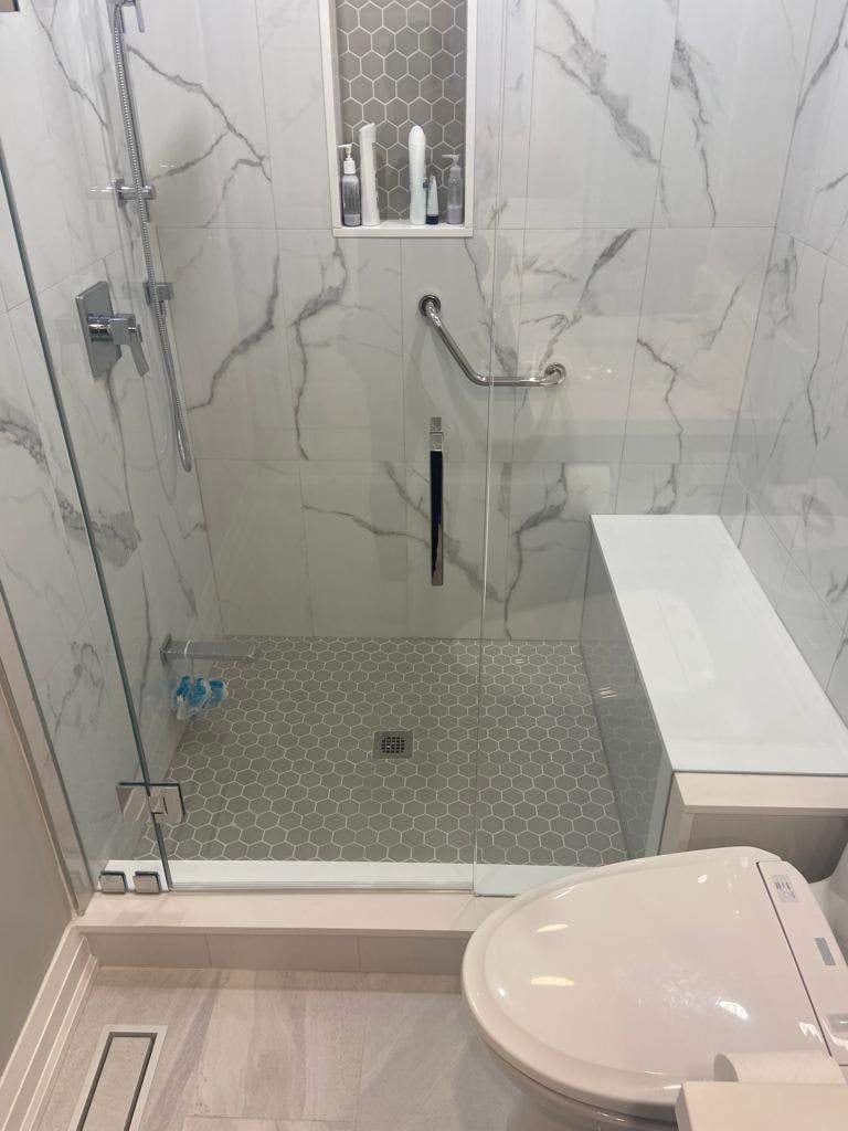 Marble-look tiled shower with grey hex floor, built-in bench, grab bar and frameless glass door