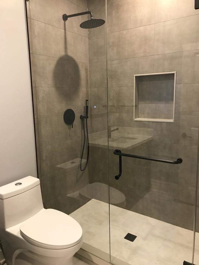 Glass shower with large grey porcelain tile, matte black rain head, grab bar and recessed niche