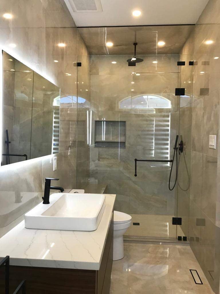 Bathroom with backlit mirror, vessel sink on a quartz vanity and glass walk-in shower with black fixtures