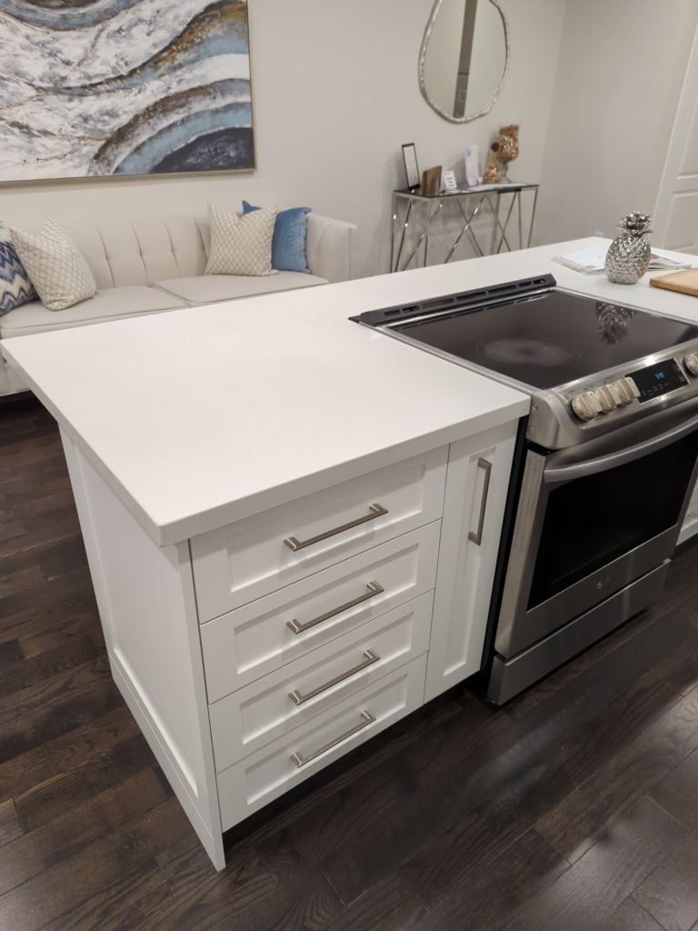 Kitchen island with white shaker drawers, quartz top and slide-in stainless range on dark hardwood