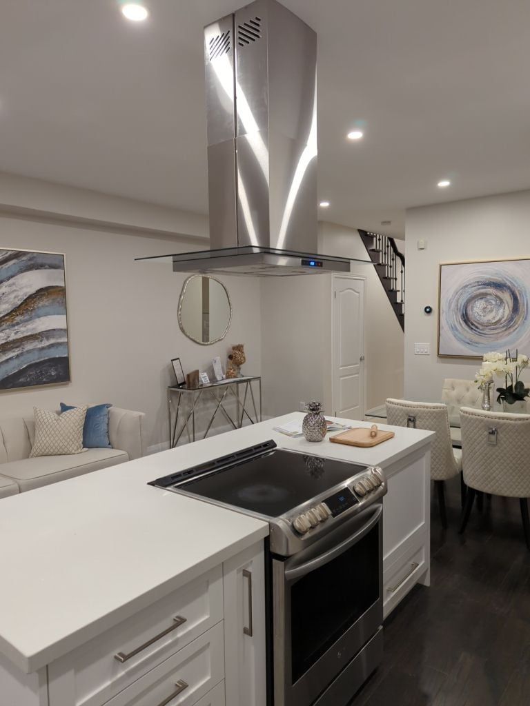 Stainless island range hood with glass canopy above a white quartz island and slide-in range