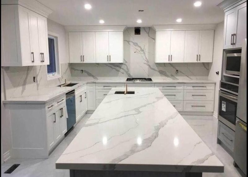 White shaker kitchen with a long quartz island, slab backsplash and stainless wall ovens
