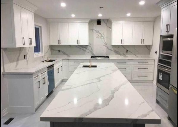 White shaker kitchen with a long quartz island, slab backsplash and stainless wall ovens