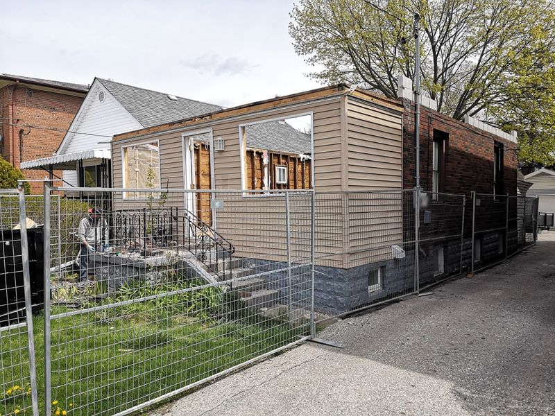 A one storey house shell without a roof or windows, behind a site fence