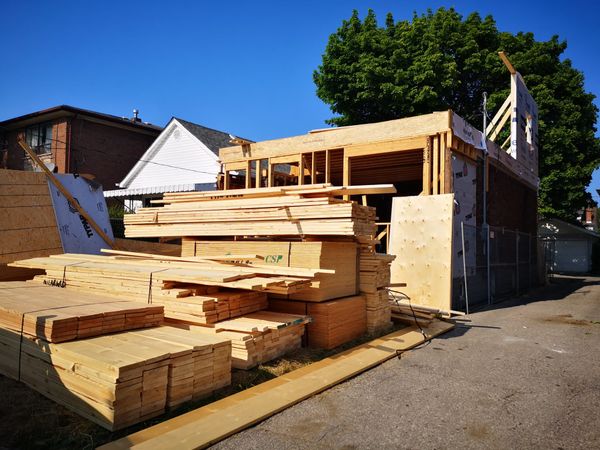 A wood frame at the back of a house, behind stacked lumber and sheathing